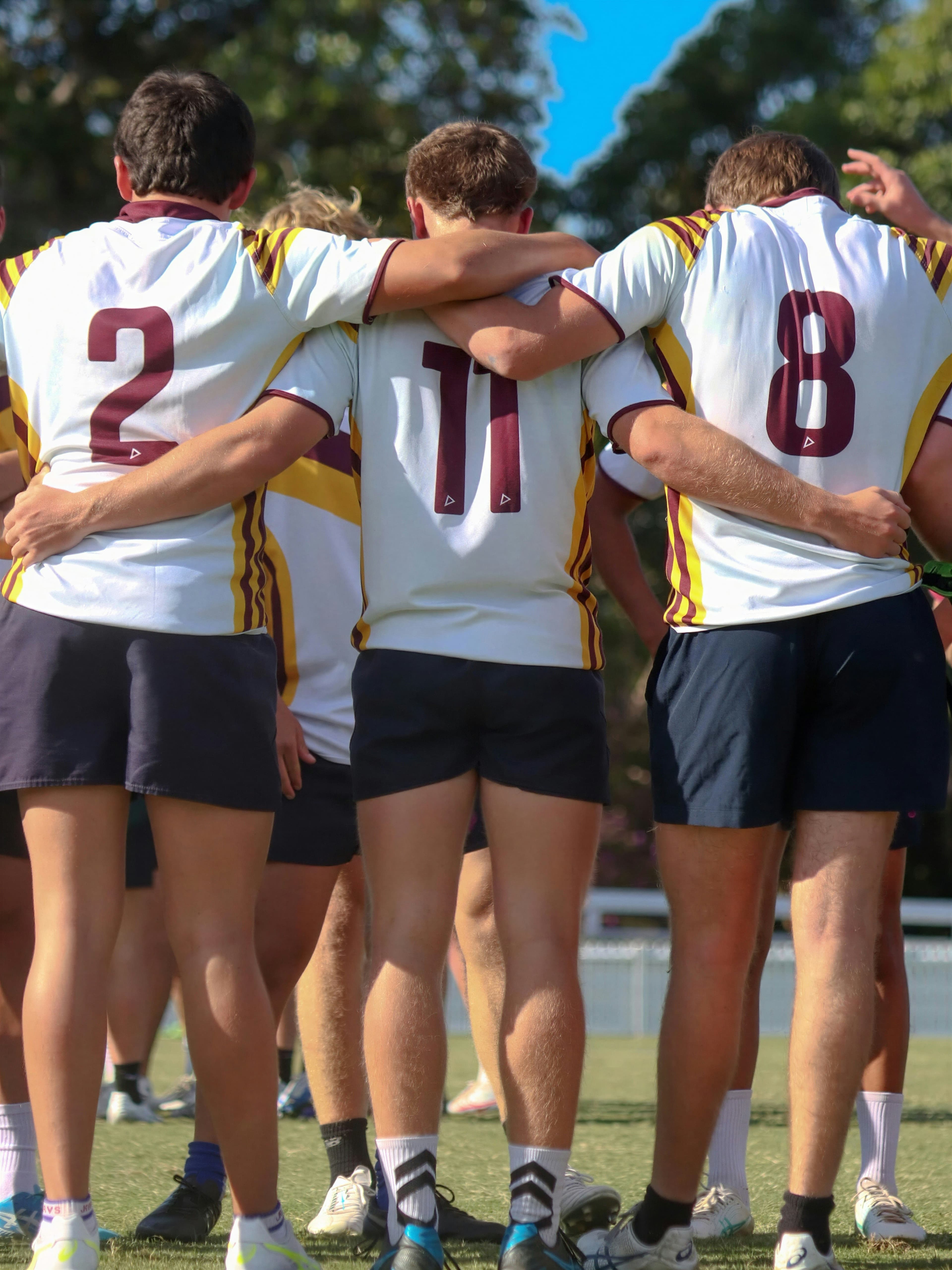 Three school rugby players in numbered jerseys, arms around each other on the field